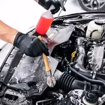 Professional detailer cleaning car engine bay with brush and foam
